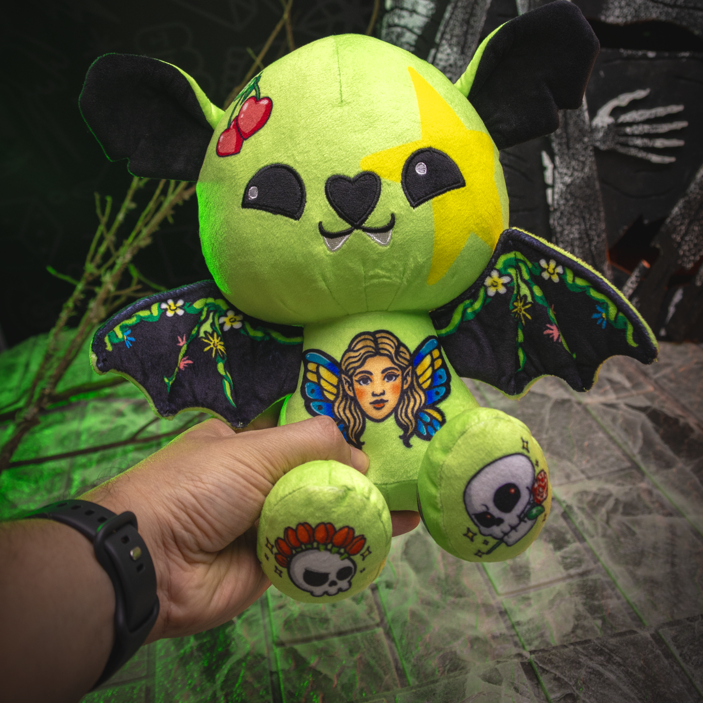 Green plush toy with bat wings and face paint held by a hand against a dark background